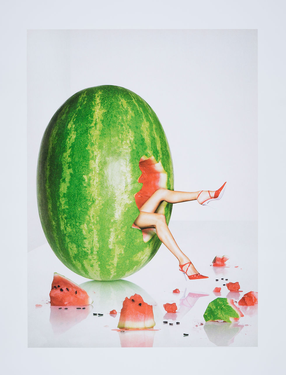 The legs of a white woman in pink high heels emerge from a large watermelon