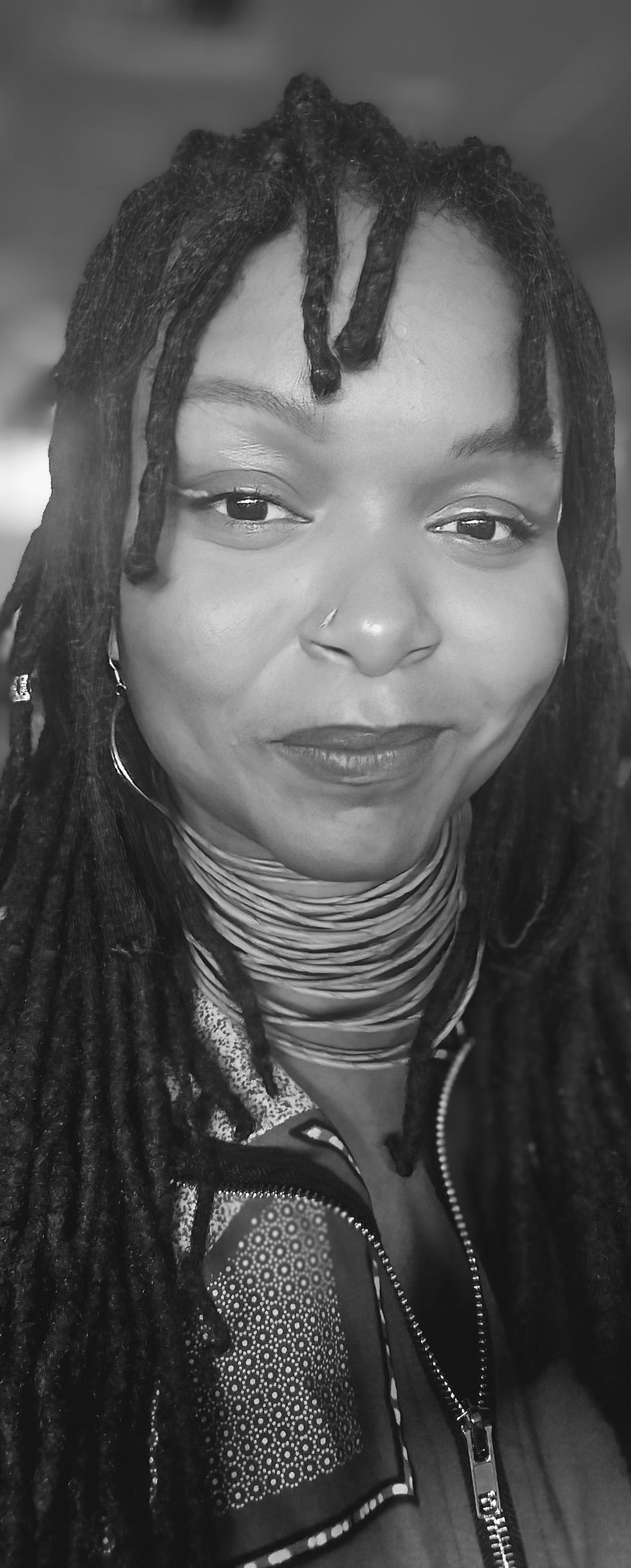 A b+w photo of a Black woman with neat, long dreadlocks in a multi wrap necklace and jewelry smiles into the camera