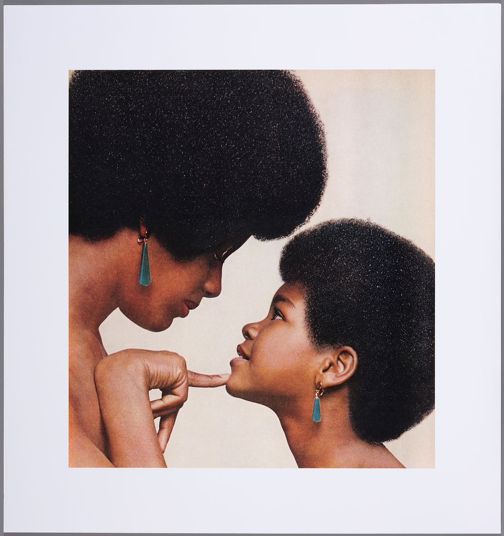 A Black woman with an afro and green dangling earrings stares lovingly into her daughter's face, with a single finger touching her chin