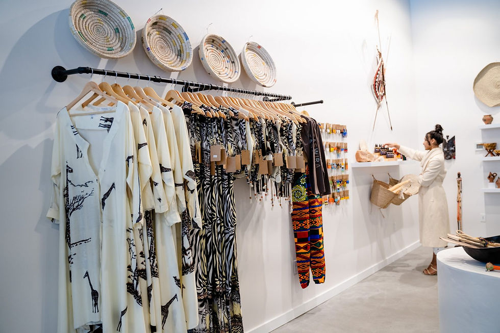 Dresses with African print hang below woven baskets on the wall of a shop selling African goods.
