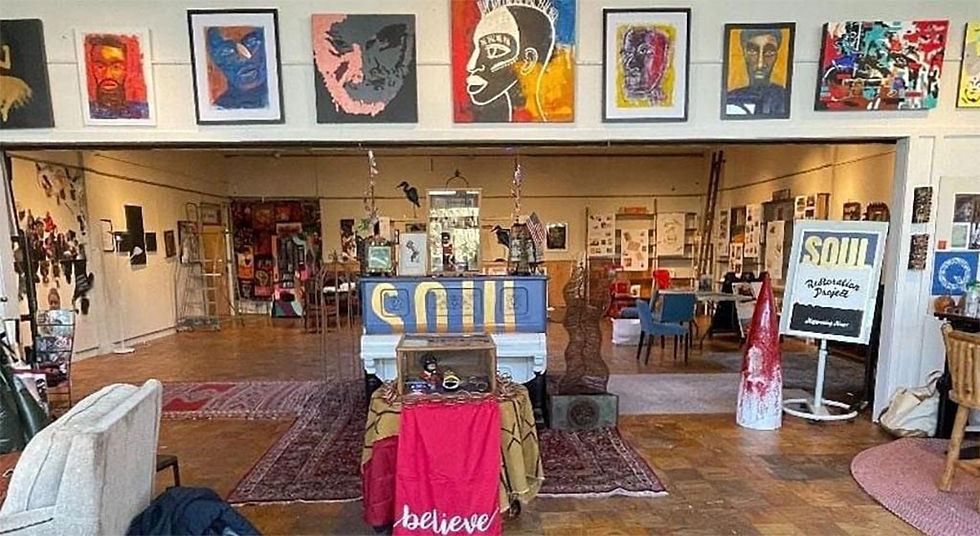 A hardwood floored room with paintings of black faces and colorful abstracts, a sign that says "SOUL" and various other arts objects