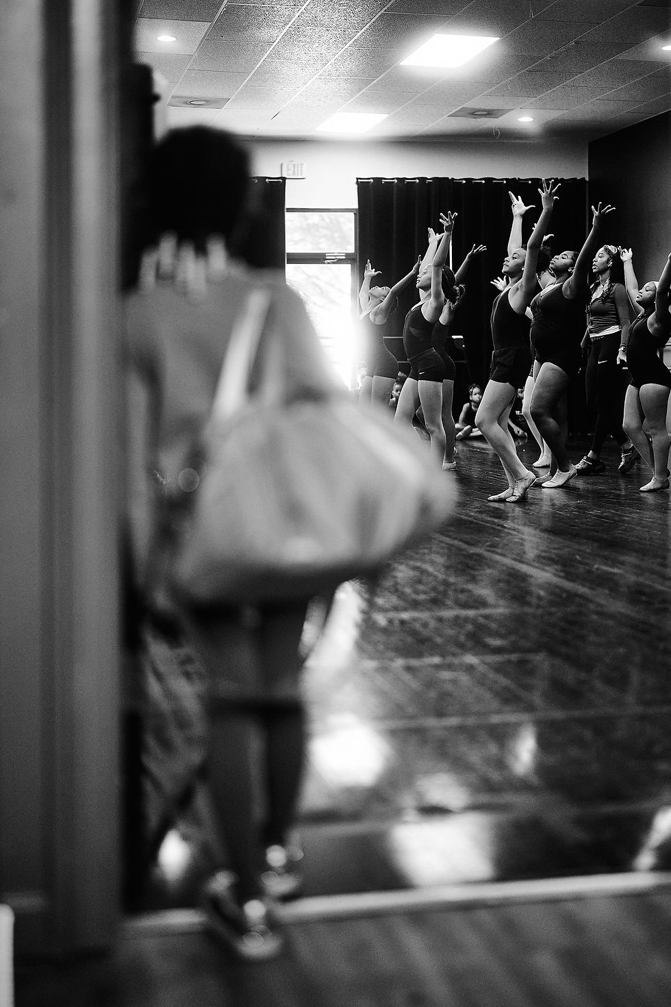 A view past a dancer in the foreground toward classmates practicing with raised arms.