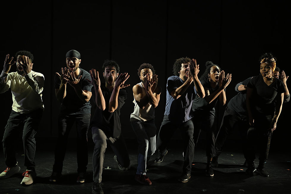 Dancers in dark clothing step forward with hands in front of their faces.
