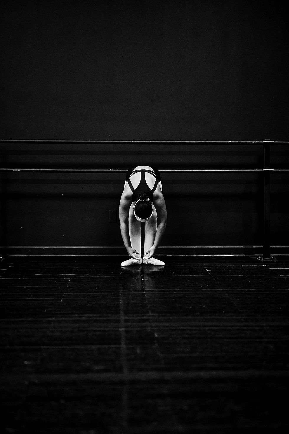 A dancer folds forward beside the studio barre.