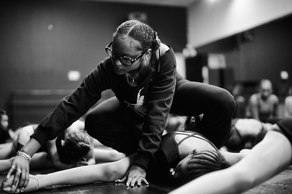 An instructor assists a dancer during a floor stretch.